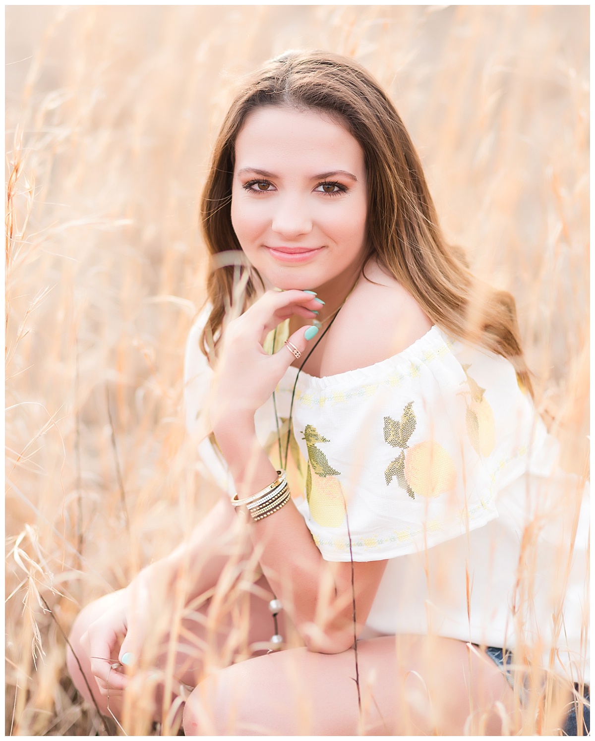 senior girl squatting in field of wheat colored grass