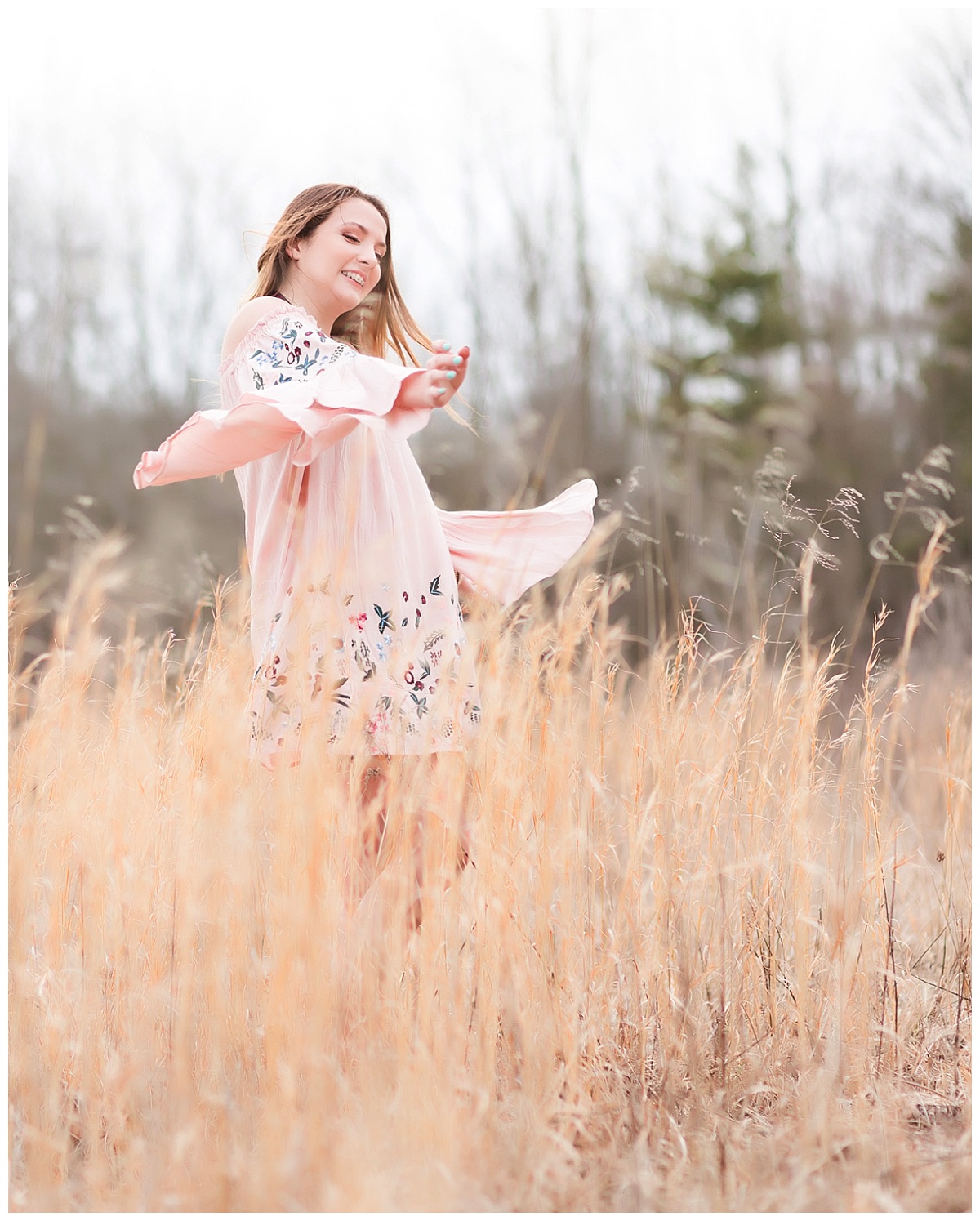 Senior girl in pink dress twirling in field of tall grass