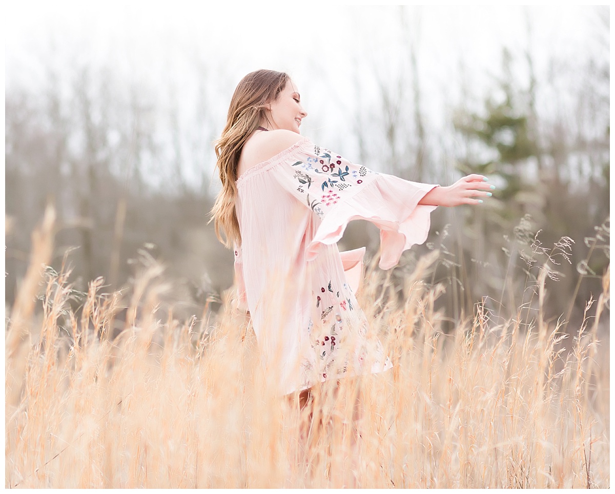 Senior girl in pink dress twirling in field of tall grass