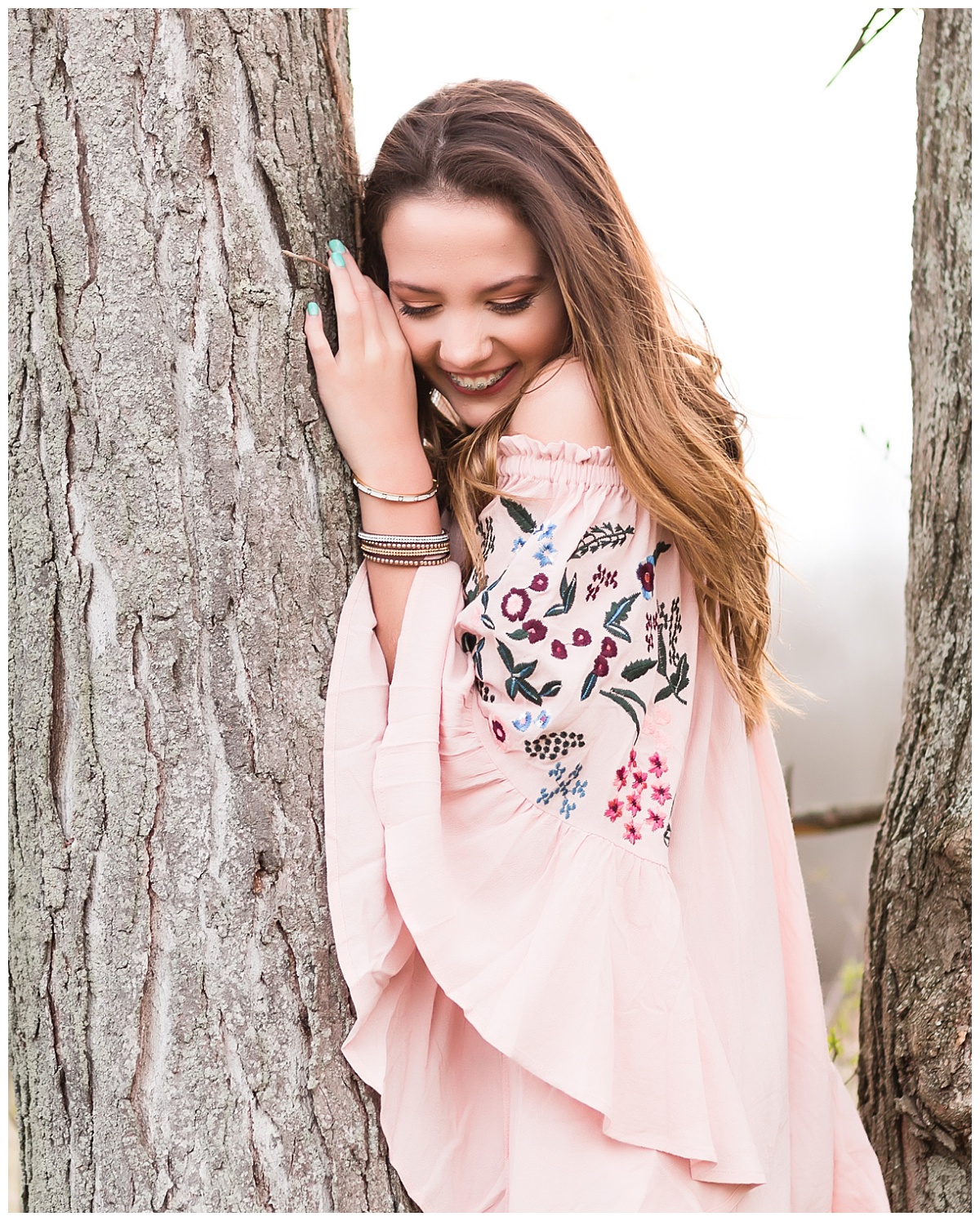 Senior girl in pink dress smiling dow standing by a tree