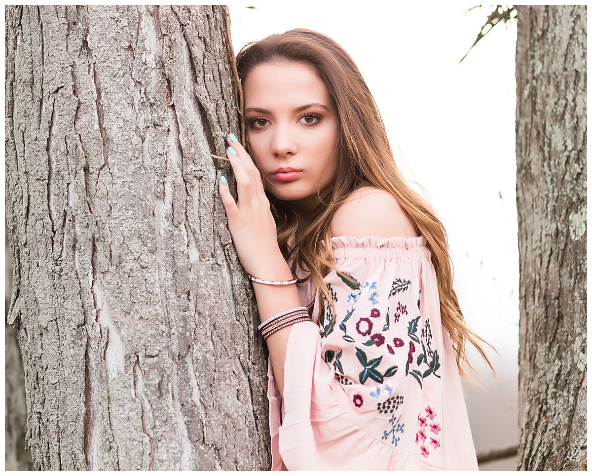 Senior girl in pink dress standing by a tree