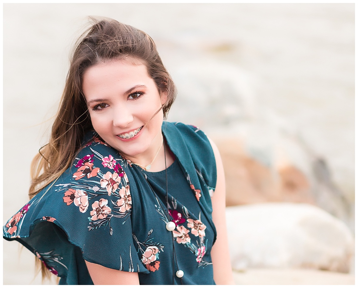senior girl smiling sitting on rocks near beach 