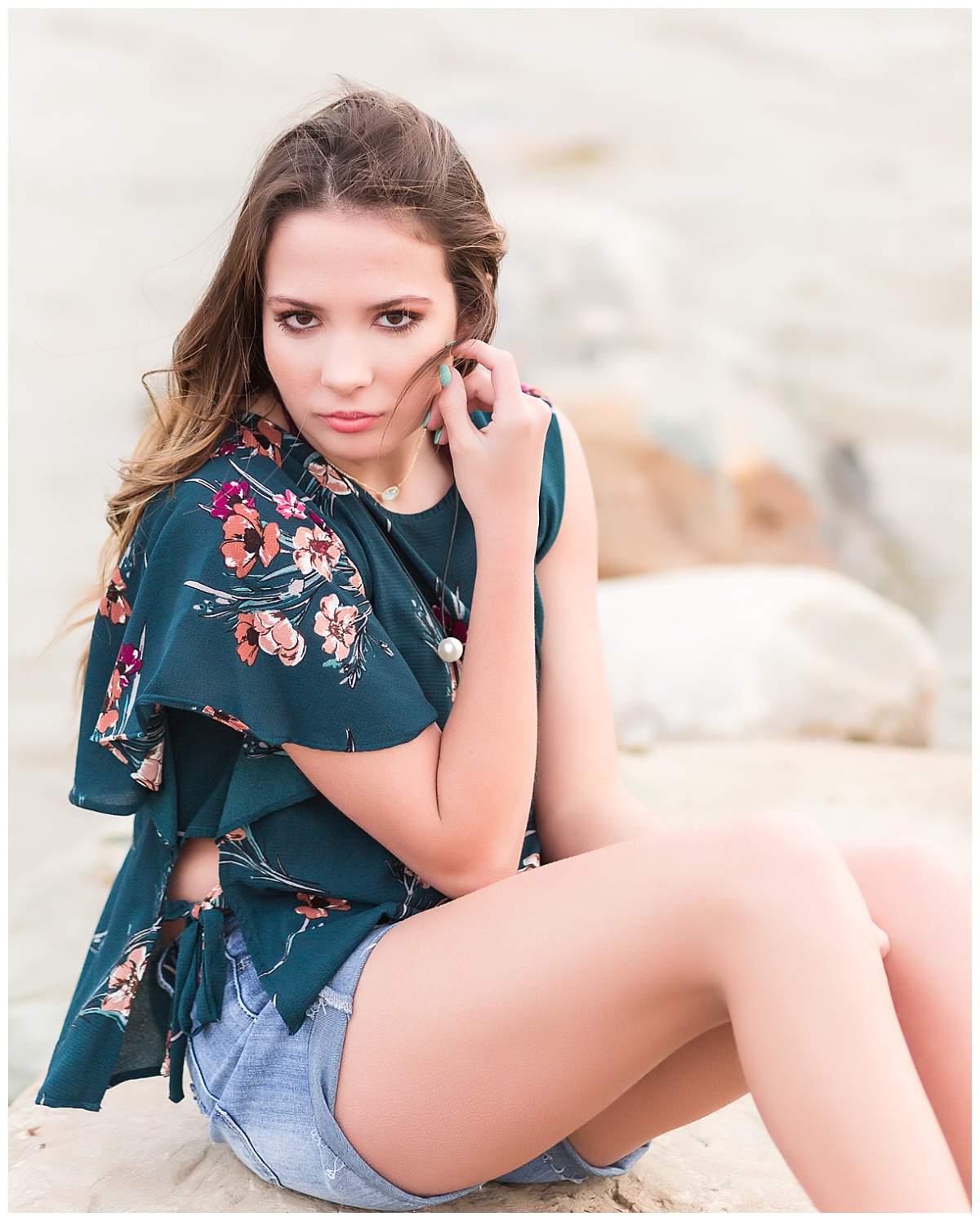 senior girl smiling sitting on rocks near beach 